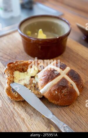 Traditional Hot Cross Bun with melted butter a traditional for Easter UK - A hot cross bun is a spiced sweet bun usually made with fruit, marked with a cross on the top, and traditionally eaten on Good Friday in the United Kingdom Stock Photo