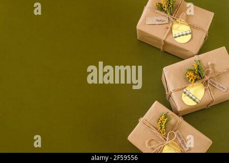 Gift boxes with an egg-shaped tag and decorated with flowers. Easter zero waste. Space for text. top view on green background.  Stock Photo