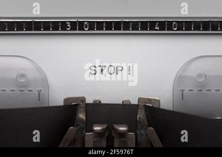 Typing text STOP on vintage manual typewriter. Close up of writes word on white paper. Shot in macro. Stock Photo