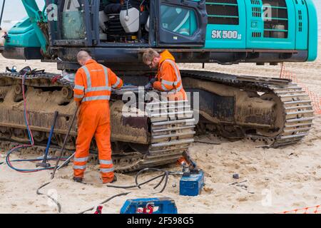 Repairing digger for beach replenishment work at Bournemouth and Poole beaches, Dorset UK in March - moving track link to carry out repairs Stock Photo