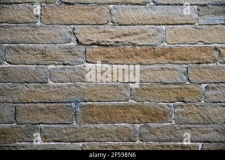 Yellow and grey stone wall with uneven sized brick work and white mortar. Stock Photo