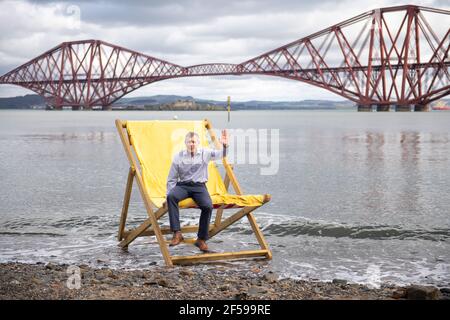 South Queensferry, Scotland, UK. 25th Mar, 2021. PICTURED: Willie Rennie MSP. Willie Rennie MSP - Leader of the Scottish Liberal Democrat Party (Scottish Lib Dems) joined by Edinburgh Northern and Leith candidate, Rebecca Bell and her daughter Daphne. He reads Rebecca's daughter a book on a giant beach chair with the view of the Forth Bridge behind as part of their Holyrood Elections campaign trail for the 6th May. Credit: Colin Fisher/Alamy Live News Stock Photo