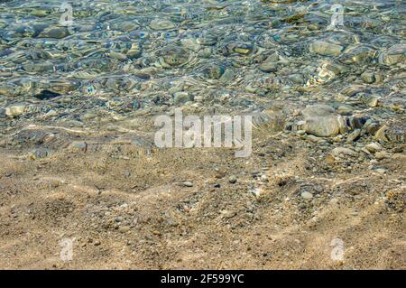 Close-up of crystal clear sea water with stones near beach on Corfu island in Greece. Background with light refraction on transparent water surface Stock Photo