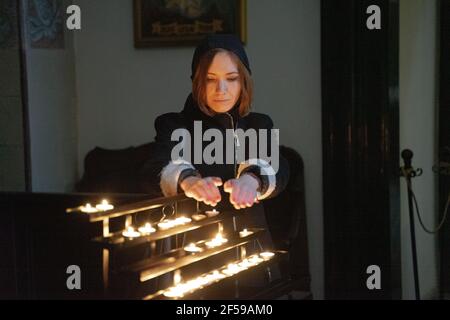 A young Caucasian woman holding her hands over round shaped tea light burning candles, concentrated face illuminated by light. Stock Photo