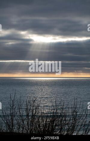 The sun shines through heavy storm clouds over a flat sea Stock Photo