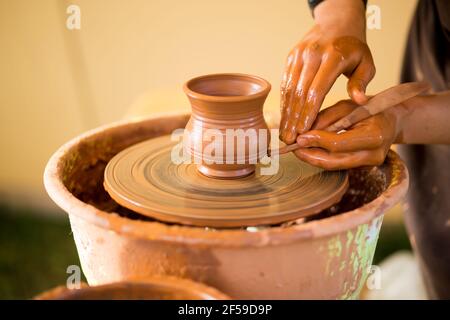 Hands of potte makes pottery dishes on potter's wheel. Sculptor in workshop makes clay product closeup Stock Photo