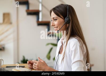 Employee girl with headphones looking at laptop computer, talking in video call working from home. Stock Photo