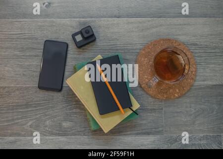 Top view on the wooden floor with books, notebook, action cam and cup of tea. Cozy, relaxing and peaceful atmosphere. Recording equipment and shooting Stock Photo