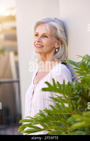 Portrait of older woman leaning on wall outside smiling Stock Photo