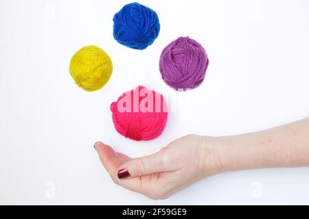 Multi-colored balls of wool yarn levitating over a hand against white background Stock Photo