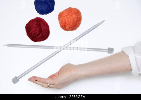 Multi-colored balls of wool yarn and knitting needles levitating over a hand against white background Stock Photo