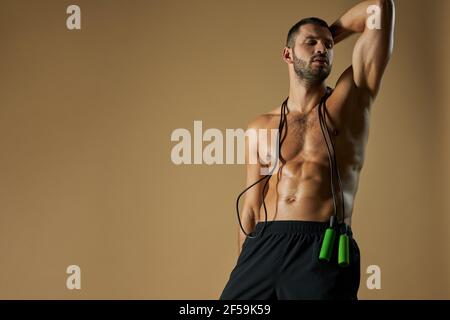 Focused adorable sportsman in black shorts looking away with skip rope on his shoulder isolated on yellow background Stock Photo