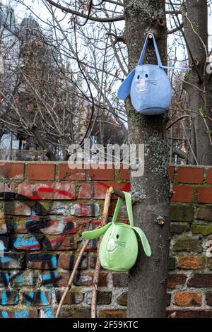 Two little felt bags with cat faces suspended from tree next to weathered brick wall, Prenzlauer Berg, Berlin Stock Photo