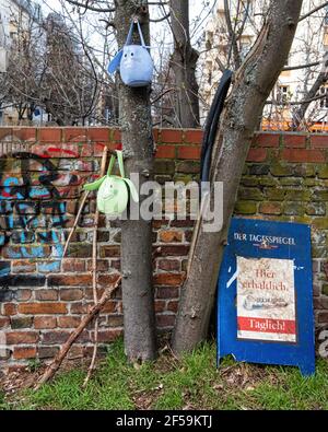 Two little felt bags with cat faces suspended from tree next to weathered brick wall, Prenzlauer Berg, Berlin Stock Photo