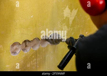 worker drilling hole for electrical socket in concrete brick wall. wiring renovation Stock Photo