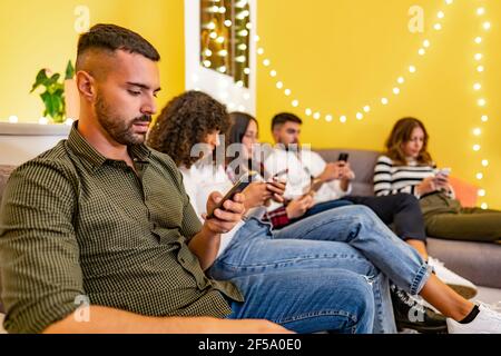 Group of serious young student friends at home sitting on the couch spend time using smartphones without real interaction between them. New social and Stock Photo
