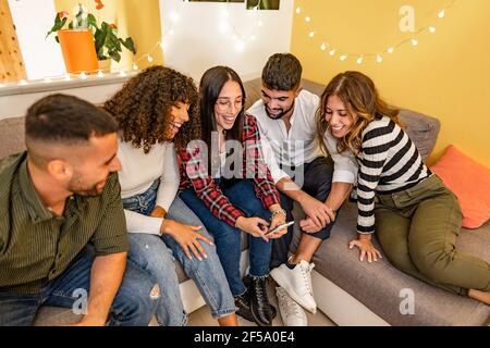 Group of young student friends at home sitting on the couch having fun with social network sharing happy moments online using smartphones. New social Stock Photo