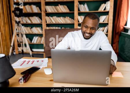 Happy male employee or student is having a video meeting with friends or colleagues, smiling. Joyful young adult businessman is working from home Stock Photo