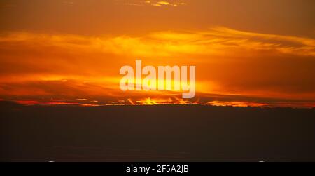 The red morning sun is covered with clouds. Dramatic sky, the flame of the sun's rays in the sky. Stock Photo