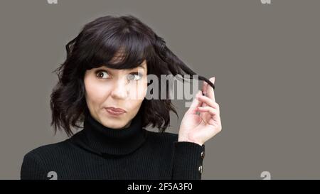 Woman flirting purses her lips while holding lock of her hair with her hand. Stock Photo