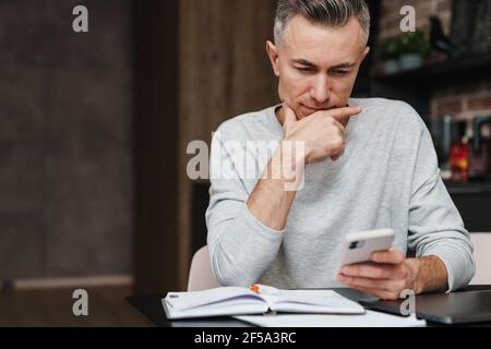 Focused handsome man using mobile phone while working at home Stock Photo