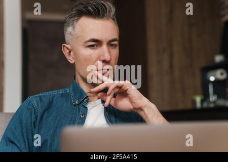 Focused handsome man using laptop while sitting on couch at home Stock Photo