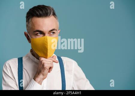 Caucasian grey-haired man in face mask thinking and looking aside isolated over blue background Stock Photo