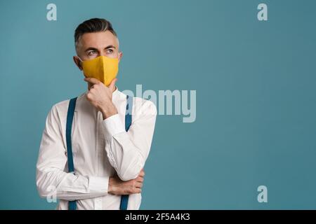 Caucasian grey-haired man in face mask thinking and looking upward isolated over blue background Stock Photo