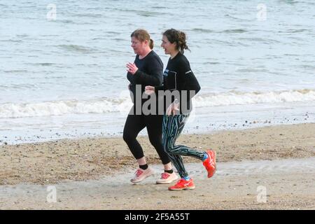 Weymouth, Dorset, UK.  25th March 2021.  UK Weather.  Two joggers out exercising on the beach enjoying the warm afternoon sunshine at Weymouth in Dorset during the Covid-19 lockdown.  Picture Credit: Graham Hunt/Alamy Live News Stock Photo