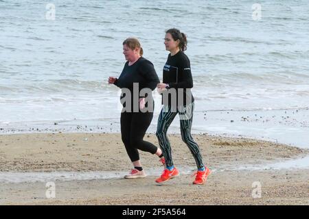 Weymouth, Dorset, UK.  25th March 2021.  UK Weather.  Two joggers out exercising on the beach enjoying the warm afternoon sunshine at Weymouth in Dorset during the Covid-19 lockdown.  Picture Credit: Graham Hunt/Alamy Live News Stock Photo