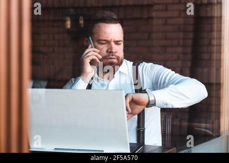Young businessman looking at his watch, laptop on the table Stock Photo
