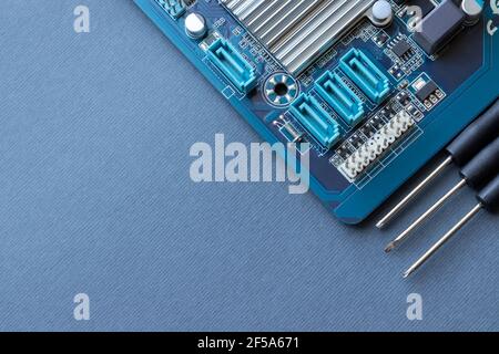 Computer motherboard and three small screwdrivers on a gray paper background with copy space Stock Photo
