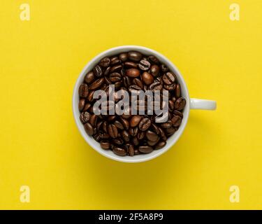 Cup of coffee with coffee beans on yellow background. Creative minimal coffee drink concept. Stock Photo
