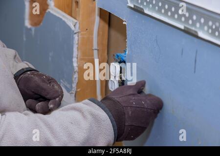 Replacement of the old outlet with a new one in closeup of hand of electrician on wall during demolition Stock Photo