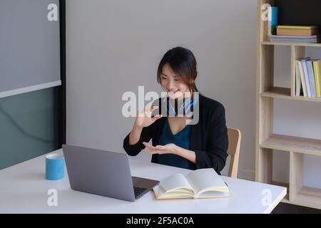 Happy young asian business woman with headphone to greeting or presentation to partner during making video conference with her team. Stock Photo