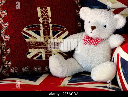 Photo of a white teddy bear on a large armchair covered in large British union jack patterned material and crown cushion with heart shaped union jacks Stock Photo