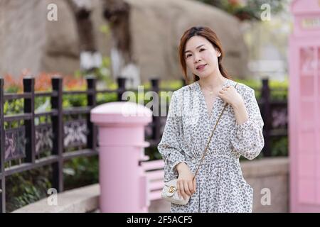 Huzhou, China 24 March 2021: Beautiful young Chinese girl wearing trendy white dress standing outdoor in city at spring near blooming sakura tree Stock Photo