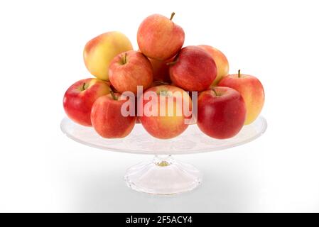 fuji apples on clear glass raised plate, red and yellow fruits isolated on white background Stock Photo