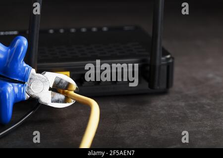 Tearing and cutting with blue wire cutters the network connection of the yellow wire of the Internet connection. Disabling and restricting Internet ac Stock Photo