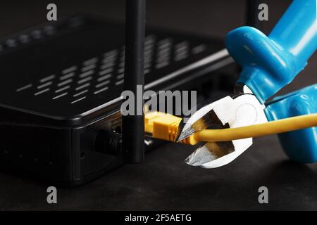 Tearing and cutting with blue wire cutters the network connection of the yellow wire of the Internet connection. Disabling and restricting Internet ac Stock Photo