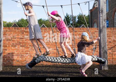 Three children, kids, sisters, girls aged / age 6 /six, 8 / eight, 10 / ten year old, playing on a rope swing operators near the historic dockyard, Chatham, Kent UK. (121) Stock Photo