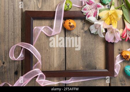 background from multi-colored flowers and painted eggs in frame with pink ribbon on wooden table. multicolored alstroemeria, pink, yellow, magenta, wh Stock Photo