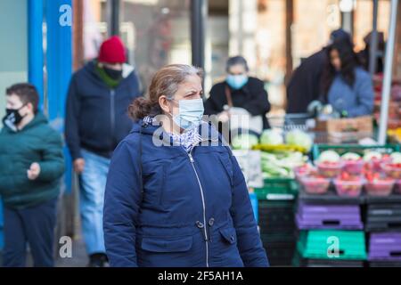 London, UK - 5 February, 2021 - a senior woman wearing a protective face mask passing by an outdoor produce market on Wood Green high street Stock Photo