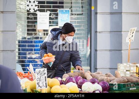 London, UK - 5 February, 2021 - A black woman wearing a protective face mask while shopping at an outdoor produce stall on Wood Green high street Stock Photo