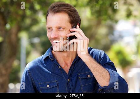 Portrait of handsome man smiling with mobile phone outdoors Stock Photo