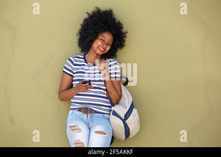 Portrait of happy woman with smart phone and bag by wall Stock Photo