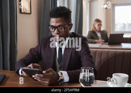 African young businessman using digital tablet while sitting at the table during lunch in cafe Stock Photo