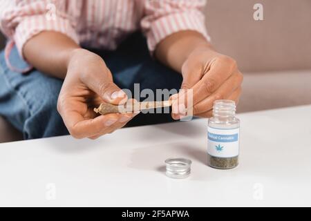 cropped view of african american woman holding rolled joint near bottle with medical cannabis lettering on table Stock Photo
