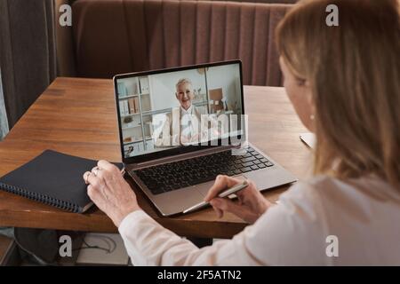 Businesswoman sitting at the table and talking with her colleague online using laptop at office Stock Photo