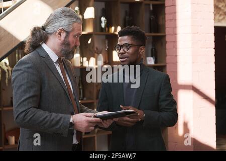 Two businessmen talking to each other and using tablet pc before meeting in the restaurant Stock Photo